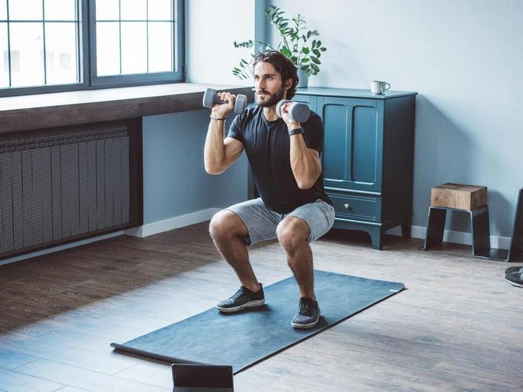 A man is doing a squat with dumbbells while looking to his right.